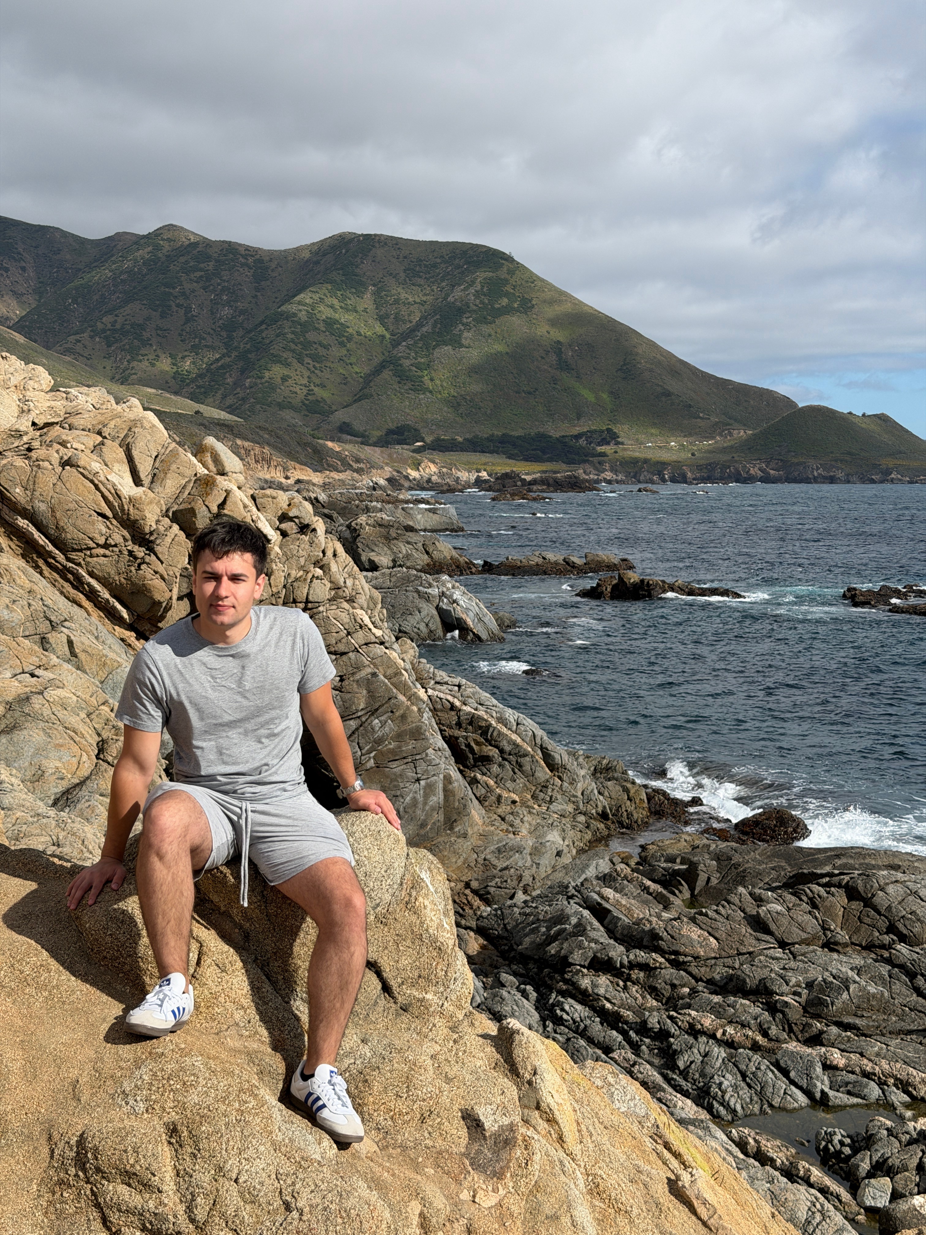 Aleks Duni sitting on coastal rocks above the ocean along the Big Sur coastline